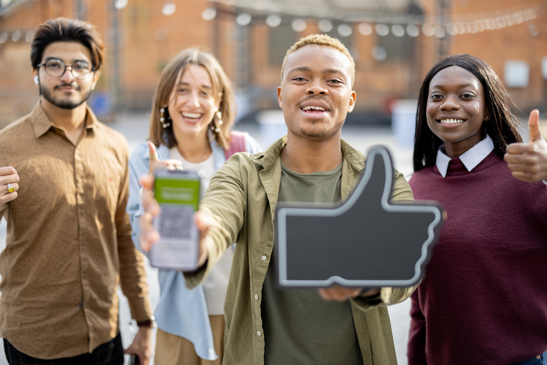 Multiracial students showing smartphone with social media and thumb up gesture