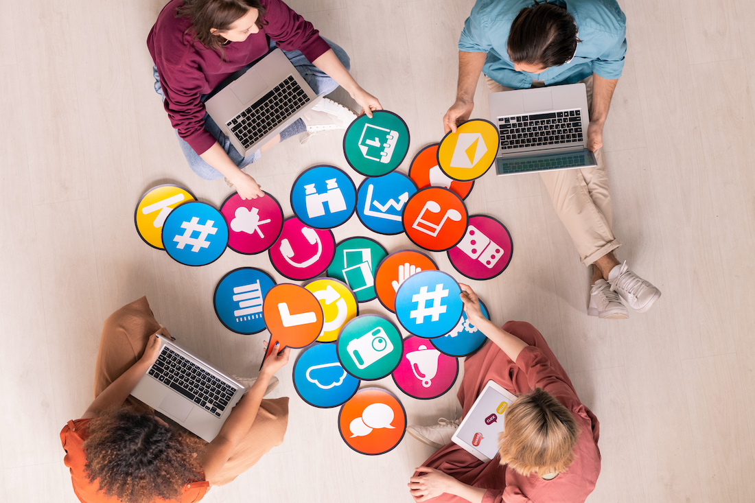 Group of friendly intercultural millennials with mobile gadgets discussing social networks icons on papers while sitting on the floor